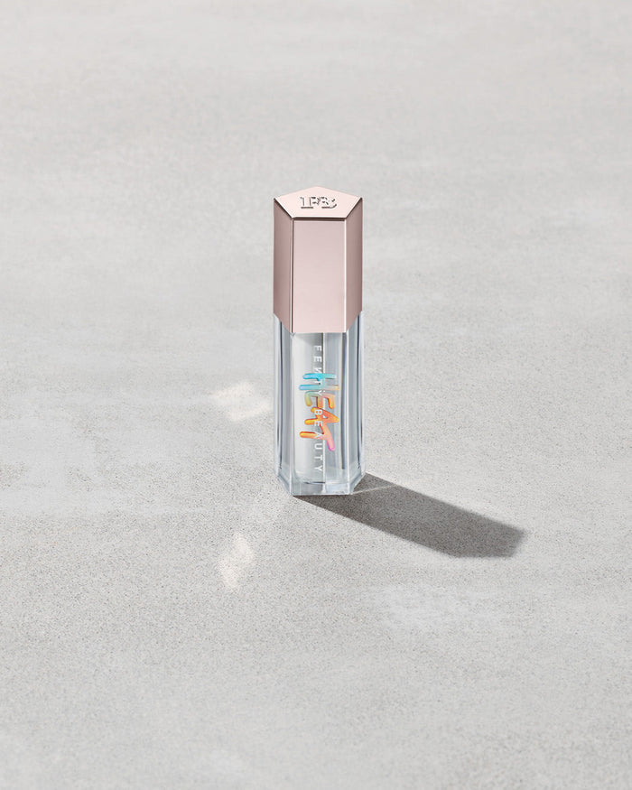 Closed tube of Gloss Bomb Heat lip gloss and plumper in the shade Glass Slipper on a grey background.