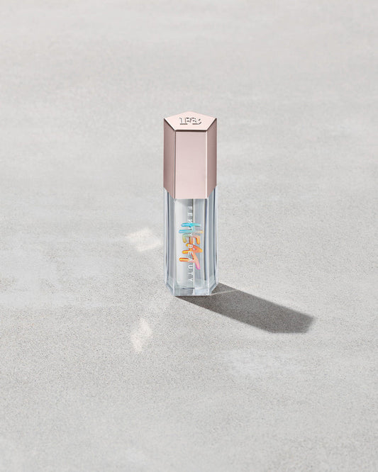 Closed tube of Gloss Bomb Heat lip gloss and plumper in the shade Glass Slipper on a grey background.