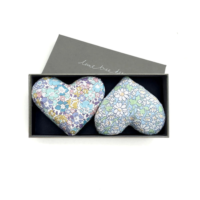 A rectangular gray box with a partially open lid reveals two HEARTS - SENTIMENTAL SACHET by LIME TREE COLLECTION LTD in pastel blue/purple and blue/green floral patterns—a charming handmade gift on a dark background.