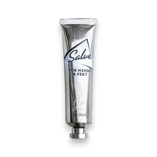 A metallic, recyclable tube labeled “JAO BRAND - SALVE FOR HANDS AND FEET” from JAO LIMITED stands upright on a white background with a silver cap and appears partially squeezed, suggesting its nourishing blend of essential oils.