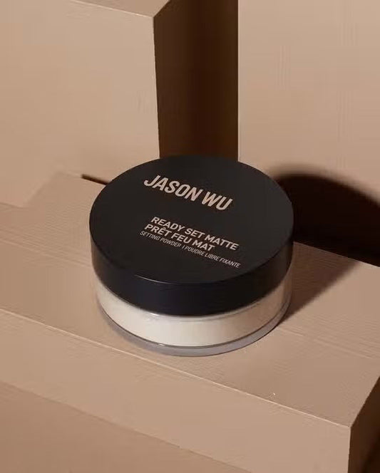 A black, round JASON WU BEAUTY container labeled "READY SET MATTE 2" rests on a beige geometric background. The clear base displays translucent setting powder inside, ideal for a flawless matte finish.