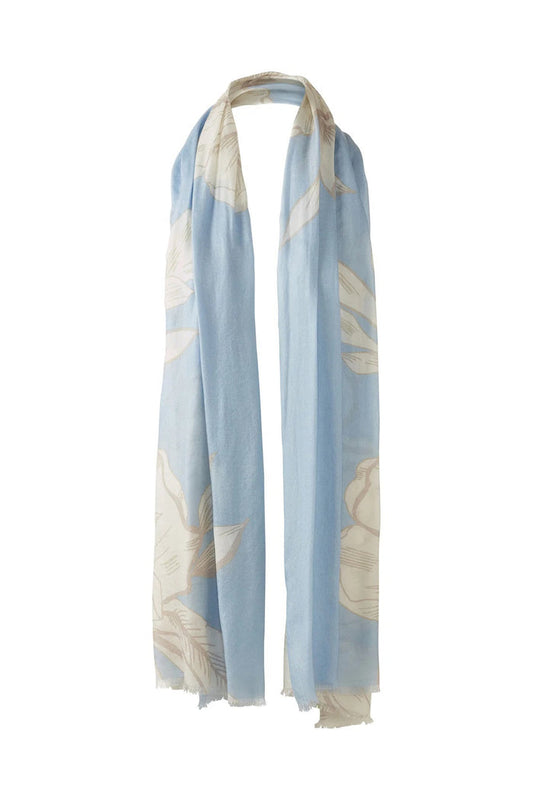 The KINROSS CASHMERE - OVERSIZED BLOOMS CASHMERE SCARF by KINROSS is a light blue cashmere scarf with a cream floral print, soft lightweight feel, and unfinished fringe edges, styled in a loop as if hung on a hook.