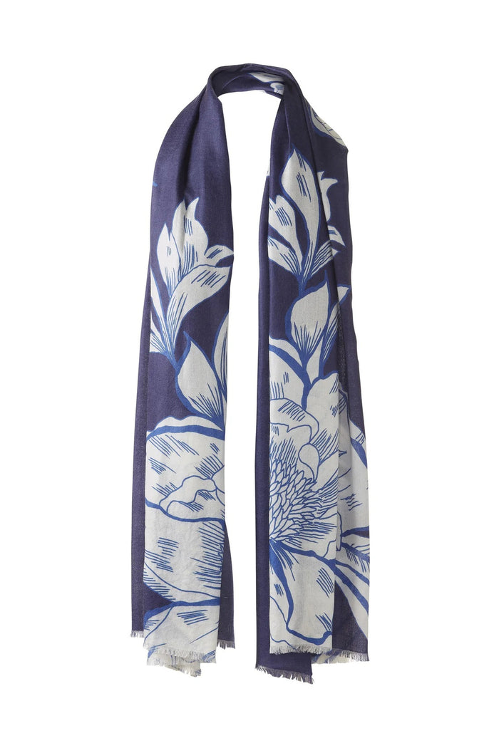 The KINROSS CASHMERE - OVERSIZED BLOOMS CASHMERE SCARF by KINROSS is a light blue cashmere scarf with a cream floral print, soft lightweight feel, and unfinished fringe edges, styled in a loop as if hung on a hook.