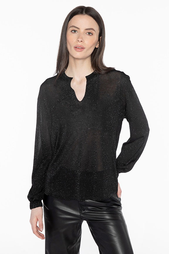 A woman with long brown hair wears the KINROSS CASHMERE SHIMMER SPLITNECK TOP, a semi-sheer black blouse with subtle lurex sparkles, paired with black leather pants against a plain white background.