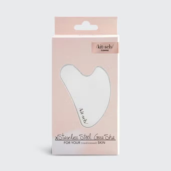 The KITSCH Stainless Steel Gua Sha comes in sleek, heart-shaped packaging with a light pink shade and a clear window. Ideal for promoting lymphatic drainage, it's branded with “/kit-sch/” and highlights benefits for stressed skin.