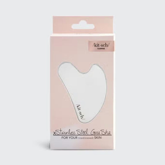 The KITSCH Stainless Steel Gua Sha comes in sleek, heart-shaped packaging with a light pink shade and a clear window. Ideal for promoting lymphatic drainage, it's branded with “/kit-sch/” and highlights benefits for stressed skin.