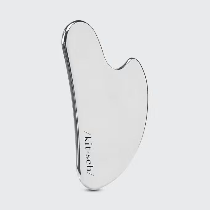 The KITSCH Stainless Steel Gua Sha comes in sleek, heart-shaped packaging with a light pink shade and a clear window. Ideal for promoting lymphatic drainage, it's branded with “/kit-sch/” and highlights benefits for stressed skin.