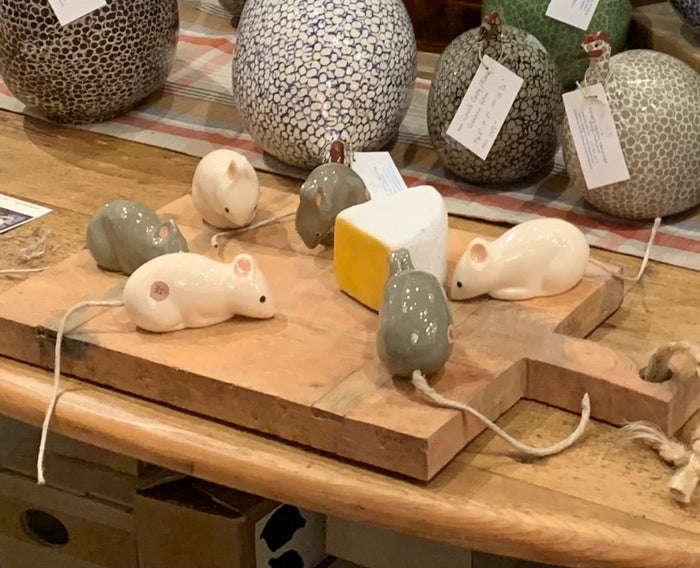 The LES CERAMIQUES DE LUSSAN - GREY LYING DOWN MOUSE by LES CERAMIQUES DE LUSSAN is a handmade ceramic figurine featuring a glossy gray body, a pink ear, a black eye, and a thin, straight tail, displayed on a white background.