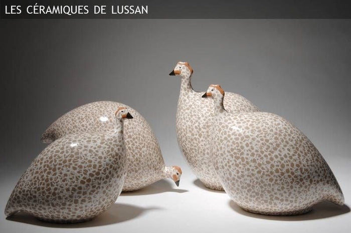 A handcrafted ceramic sculpture by LES CERAMIQUES DE LUSSAN, the Pecking Ceramic French Guinea Fowl in White Spotted Black, displays a striking black body adorned with white spots and stands on a pale cylindrical base against a minimalist white background—capturing the enduring elegance of South of France pottery.
