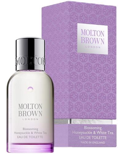 A bottle of MOLTON BROWN - HONEYSUCKLE AND WHITE TEA EAU DE TOILETTE, a delicate floral scent with bergamot notes, stands before its purple patterned box. The clear bottle is topped with a silver cap and displays simple black text.