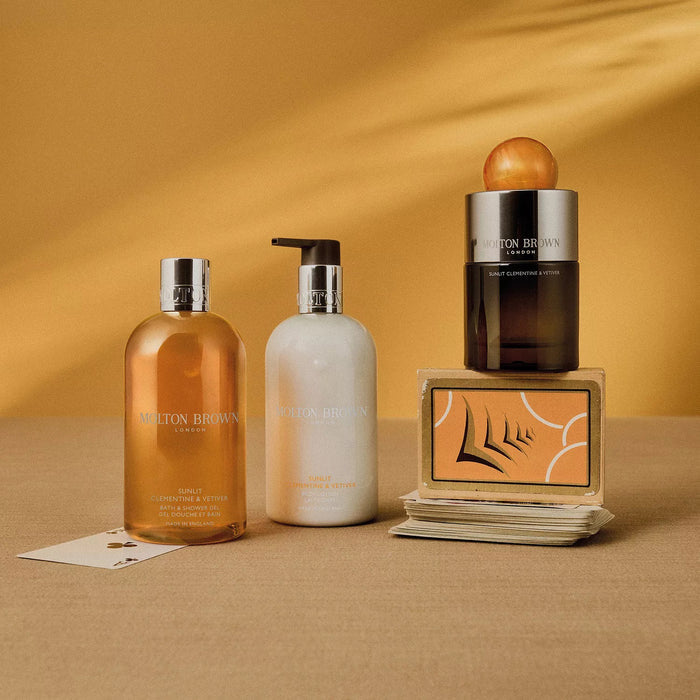 A black MOLTON BROWN SUNLIT CLEMENTINE & VETIVER Eau de Parfum bottle with a large marbled orange cap hints at citrus and vetiver notes, set against a plain white background.