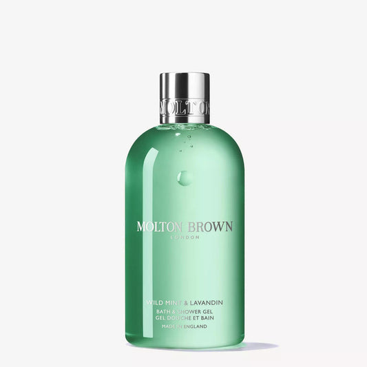 A set of MOLTON BROWN toiletries, featuring the WILD MINT AND LAVANDIN BATH & SHOWER GEL, a rollerball vial, a jar with a green sphere, and a small tin, displayed on mossy bark with a green and beige background.