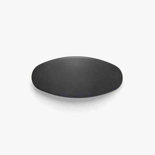 The MSCHETE - JUMBO OVAL BARRETTE IN MATTE BLACK by MACHETE is displayed against a plain white background, showcasing its simple, matte black, oval-shaped design reminiscent of a sleek oversized barrette.
