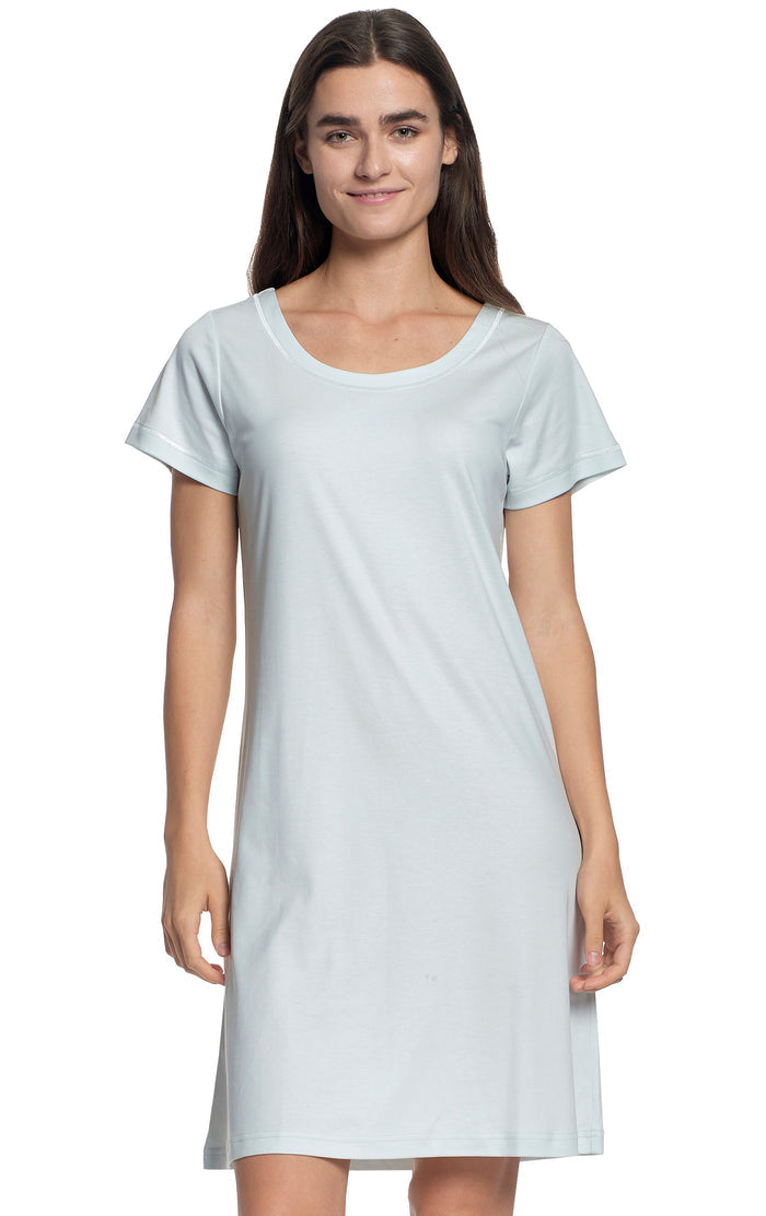 A woman with long brown hair smiles while modeling the FASHIONVIEWS P. JAMAS Butterknit Short Sleeve Gown—a light pink, knee-length pima cotton dress—against a white background.