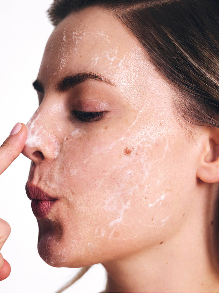 A woman gently applies a creamy face mask, focusing on her nose, highlighting skincare and self-care routine.
