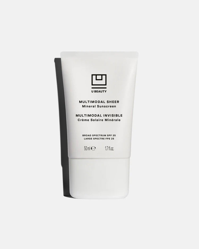 A woman with straight blonde hair wears an oversized white shirt and beige underwear, holding U BEAUTY's MULTIMODAL SHEER MINERAL SUNSCREEN BROAD SPECTRUM SPF25, ready to apply it against a plain light background.