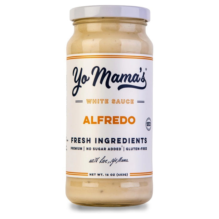 Two plates with large slices of chicken Alfredo pizza, made with fresh cream and parmesan cheese, sit beside a jar of YO MAMA'S - CLASSIC ALFREDO by YO MAMA'S FOODS, a bowl of red pepper flakes, a pizza tray, and a green napkin on a white surface.
