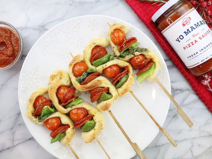 A clear glass jar of YO MAMA'S FOODS PIZZA SAUCE with a white lid showcases the No Added Sugar, keto-certified red sauce. The side label lists ingredients, nutrition facts, social media icons, and a bar code.