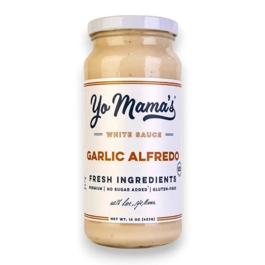 A jar of YO MAMA'S - ROASTED GARLIC ALFREDO by YO MAMA'S FOODS rests on an orange background, featuring a 16 oz (453g) label that boasts "Fresh Ingredients," "No Sugar Added," "Gluten-Free," with roasted garlic and parmesan cheese.